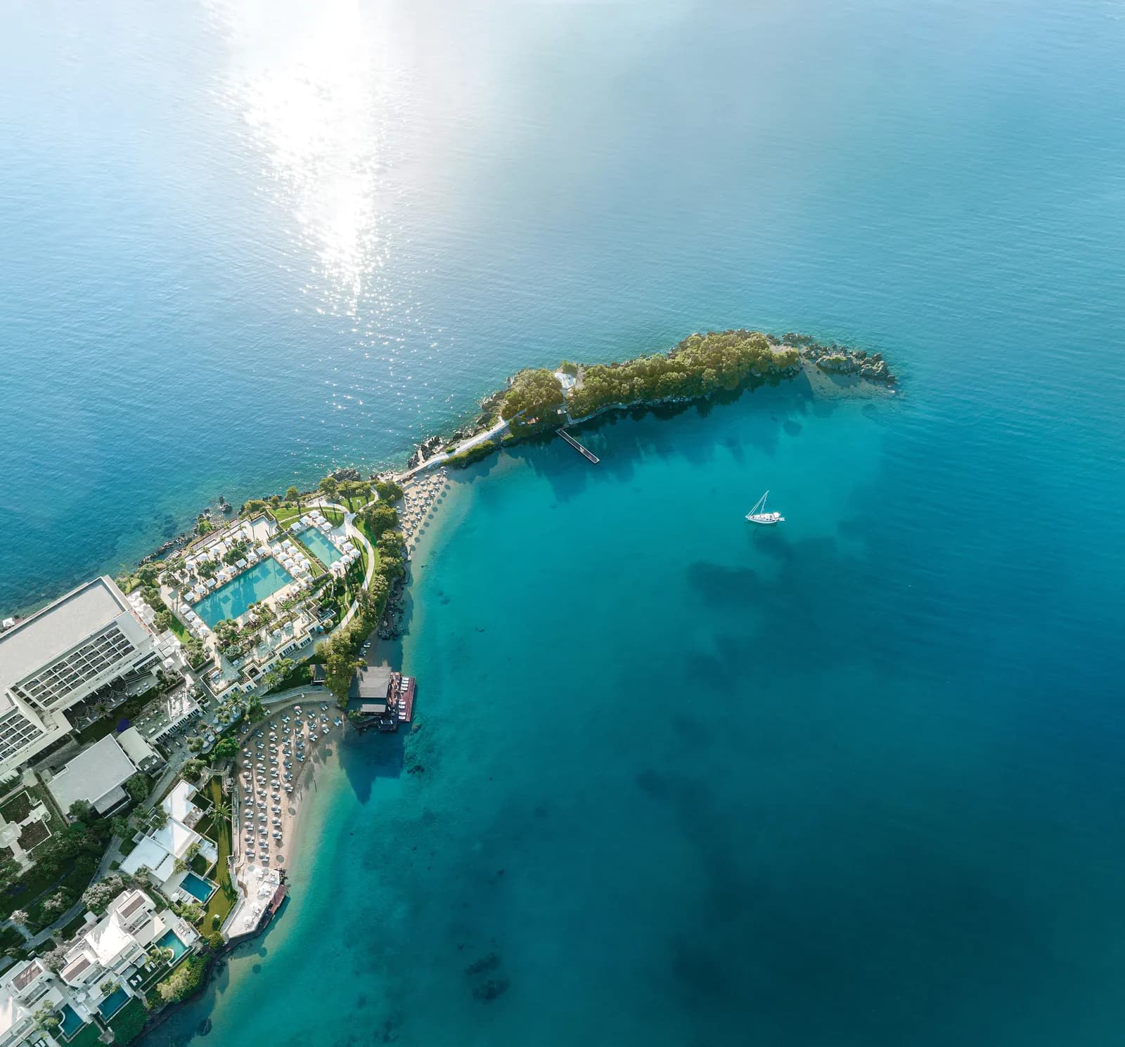 Die begrünte Halbinsel des Corfu Imperial mit einer Yacht im klarblauen Meer
