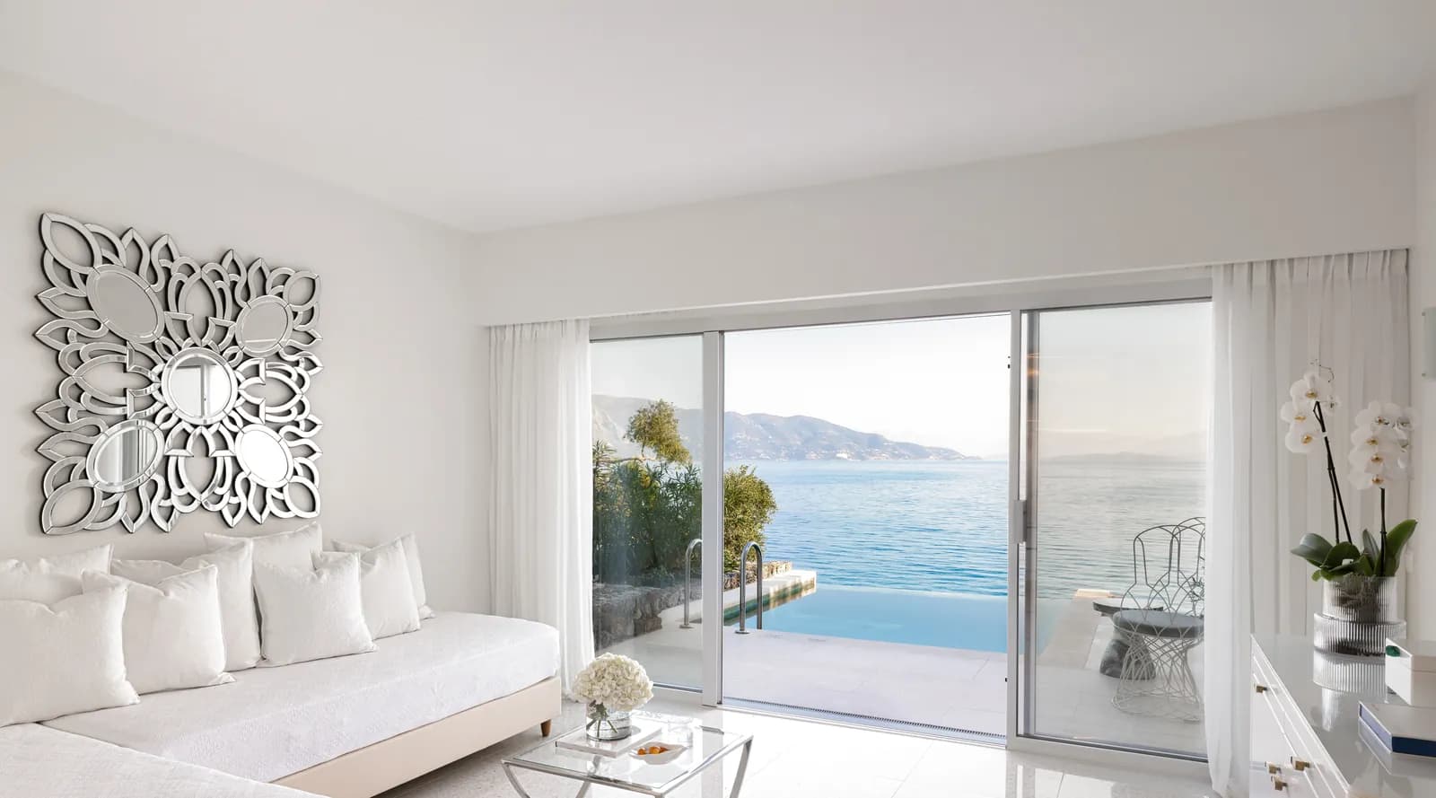 Zimmer mit Sitzbank und Blick durch die Glastür auf Pool und Meer