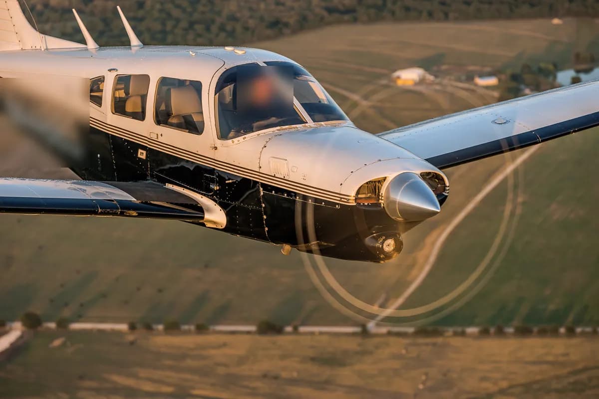 Piper PA-28 Turbo Arrow im Flug über Feldern im Abendlicht