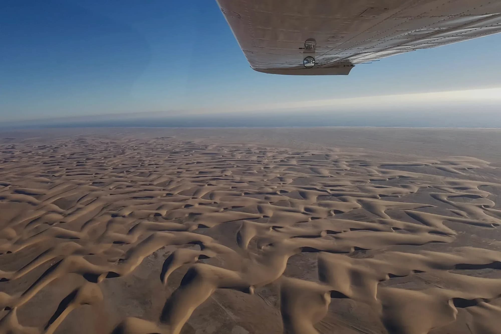 Blick über die Tragfläche einer Cessna auf die Dünen der Namib